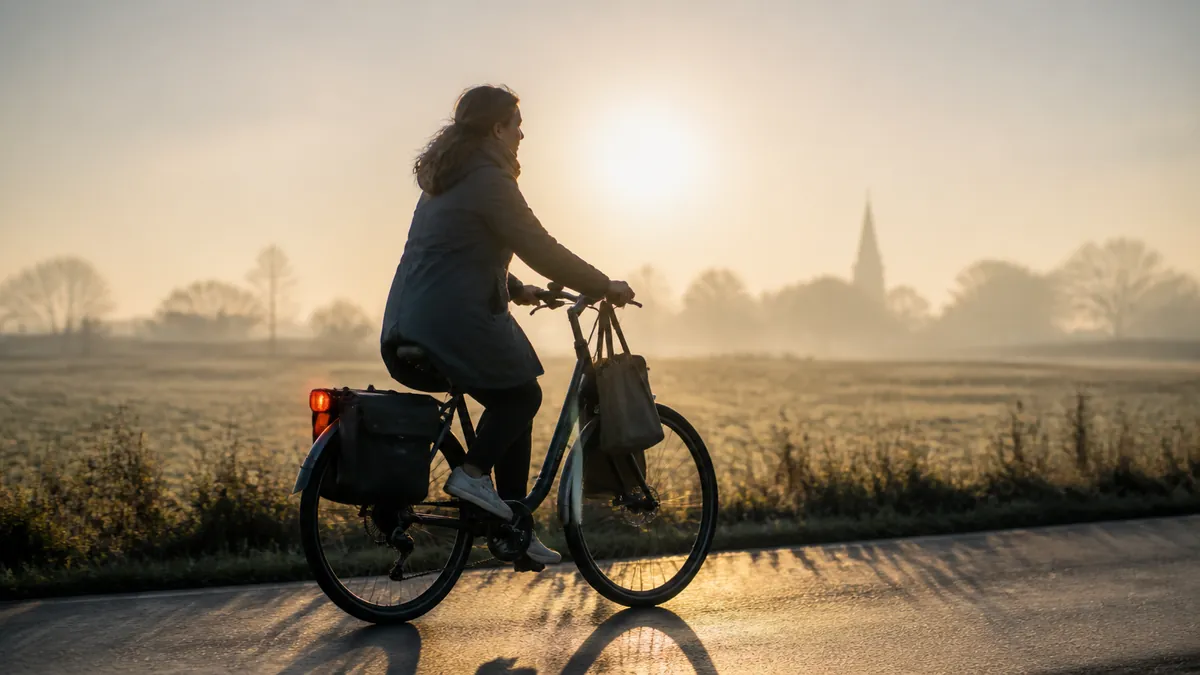 Vrouw fietst bij zonsopgang over een Vlaamse landweg naar het werk